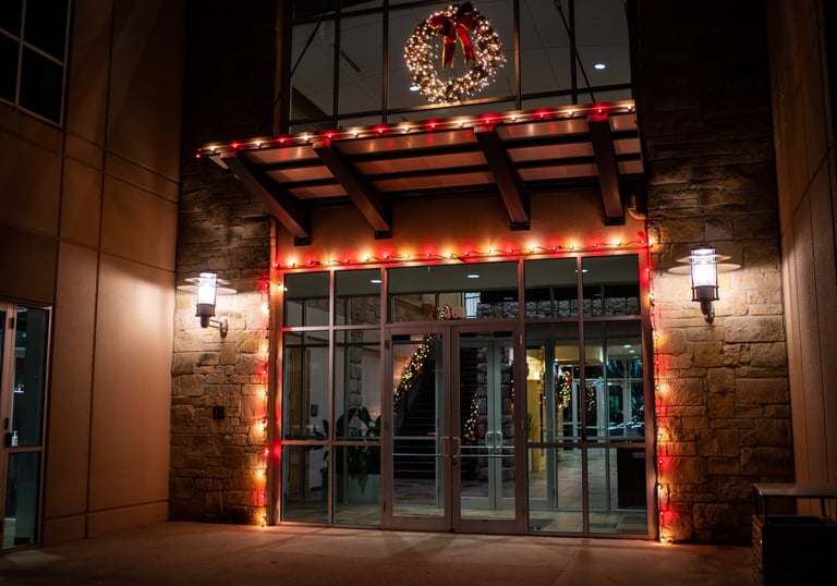Modern office building entrance decorated with red Christmas lights and a lit holiday wreath at night.