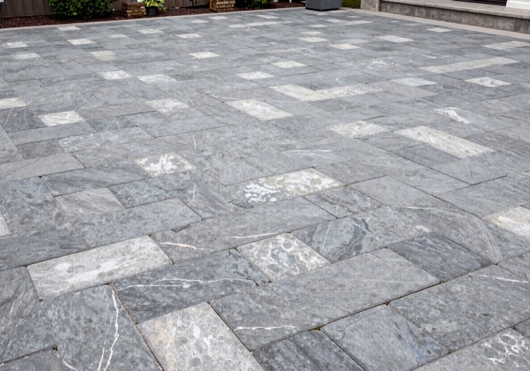 Wide shot of a luxury outdoor patio in a North American / US backyard featuring interlocking paving stones in shades of slate grey and pale cloud.