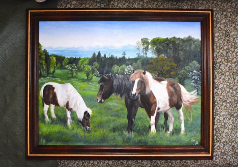 a framed painting of three horses grazing in a field
