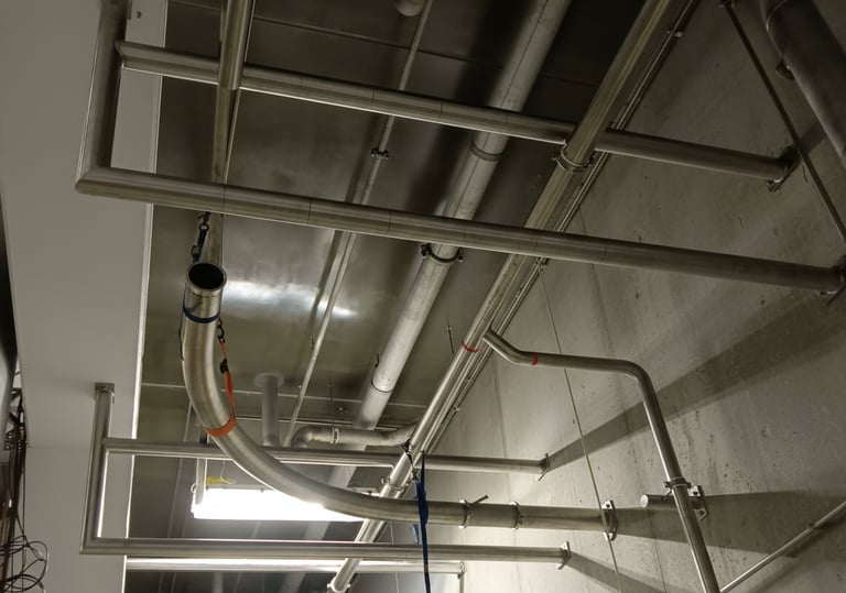 Stainless steel piping network and plumbing installed along a concrete wall.