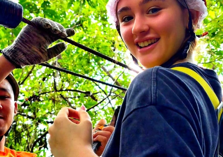 Smiling girl wearing an orange Petzl helmet and safety harness at a Hawk Adventure ropes course.