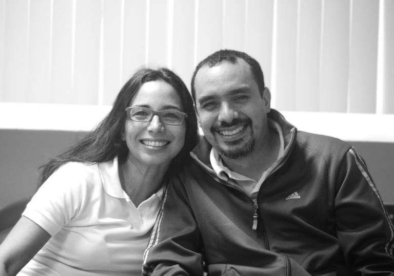 Un hombre y una mujer sentados uno junto al otro en un sofá, sonrientes miran la cámara