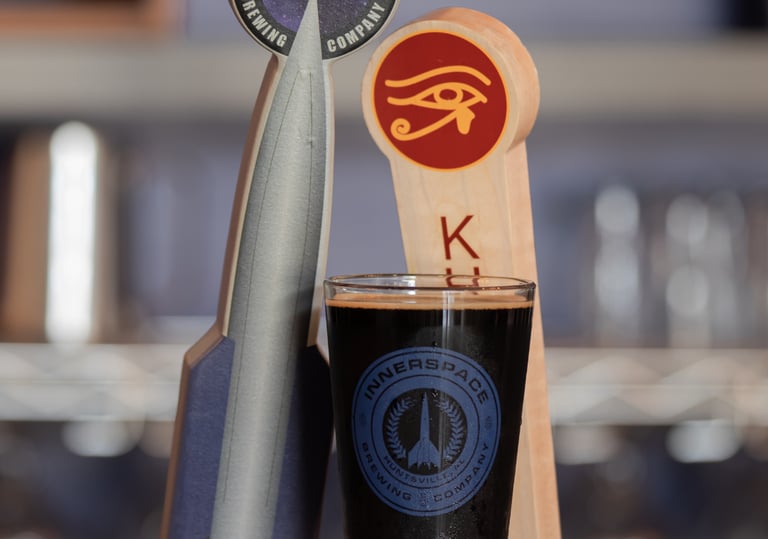 A pint of dark craft beer in an Innerspace Brewing Company glass next to a rocket-shaped tap handle.