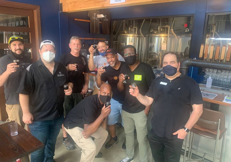 A diverse group of men wearing face masks enjoy a craft beer tasting at a local brewery taproom.