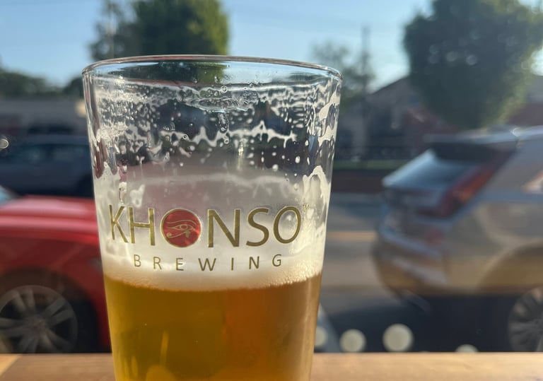 A cold pint of craft beer from Khonso Brewing sitting on a sunny outdoor patio table.