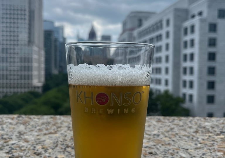 A glass of Khonso Brewing craft beer on a rooftop overlooking the Atlanta city skyline.