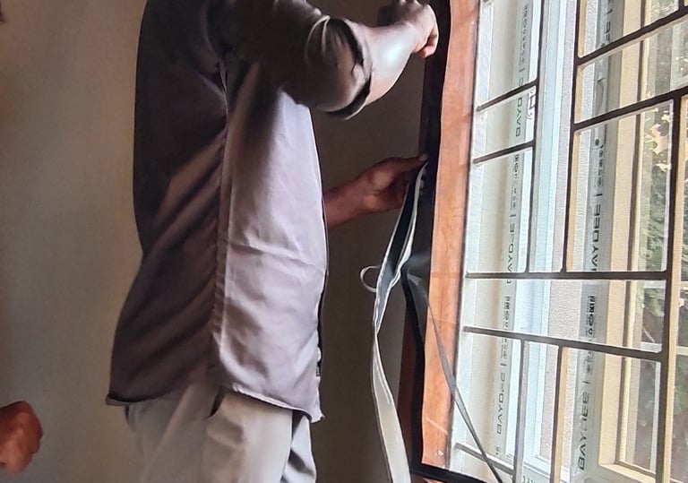 Technician carefully installing a mosquito net on a metal window frame in a Bangalore home.
