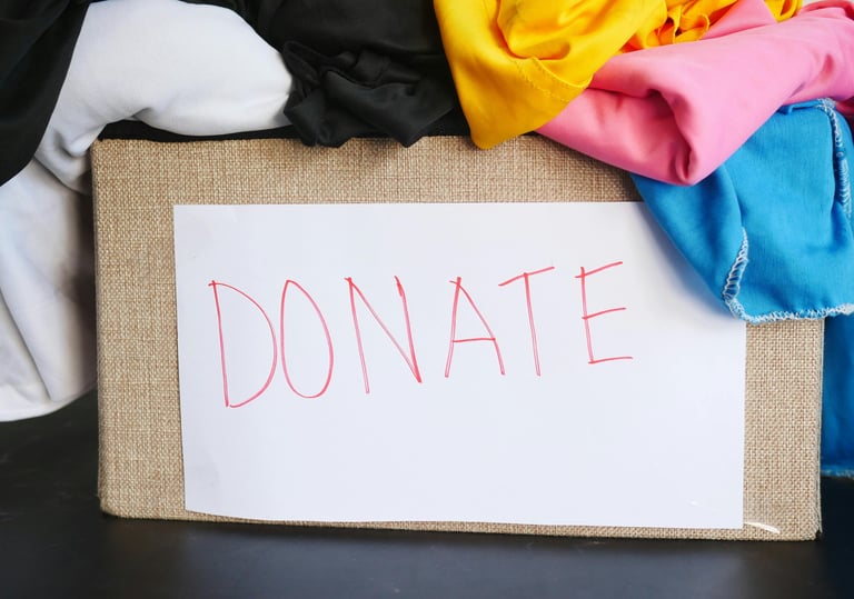 A cardboard box filled with colourful clothes for donation featuring a handwritten donate sign.