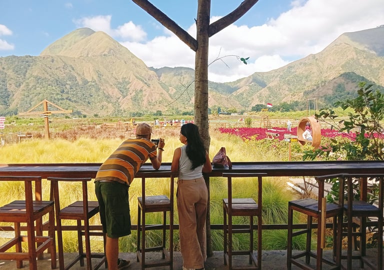 Couple taking photos of scenic mountain views and flower gardens from an outdoor cafe terrace.