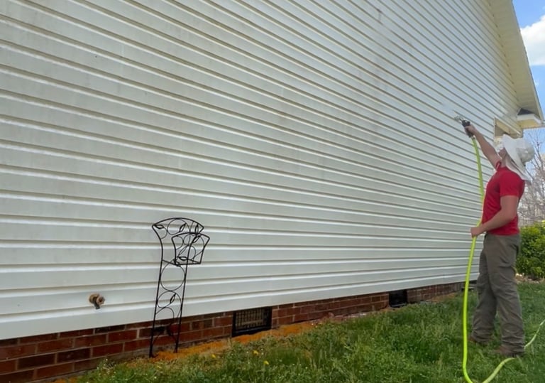 Man in gear soft washing white vinyl siding: gentle mist clears mildew, Lenoir pressure washing pro