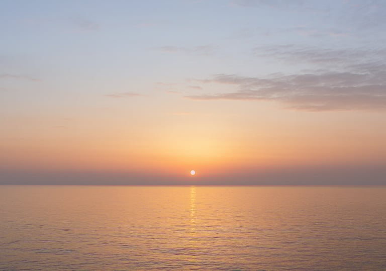 A soft sunrise over a calm sea, the sky shifting from darkness to light 