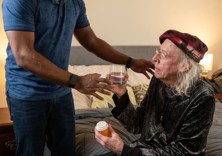 A smiling male caregiver hands a glass of water to an elderly man holding a bottle of medication