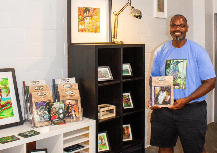 Smiling artist, David Thompson, showcasing EverLore books and colorful fantasy artwork in a modern g