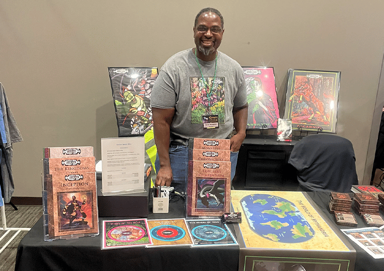 David Thompson, a smiling creator stands behind a table displaying EverLore tabletop roleplaying gam
