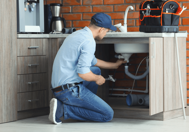 a man in a blue shirt and jeans is fixing a sink