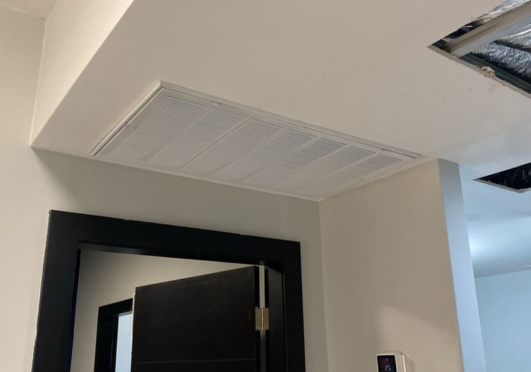 Rejilla de retorno de aire HVAC residencial blanca instalada en un plafón sobre una puerta