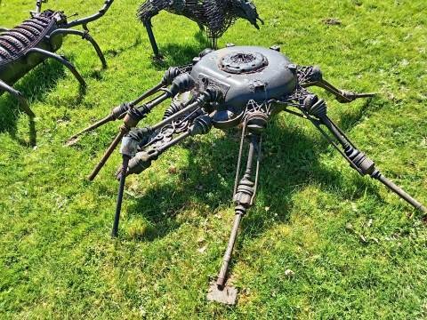 A metal spider sculpture made from recycled car parts and scrap metal on a green lawn.
