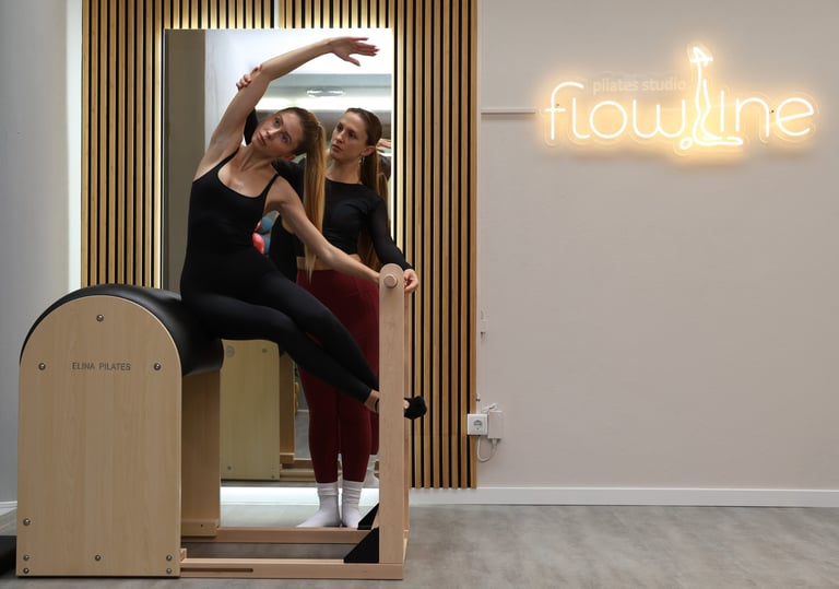 Instrutora de Pilates ajudando uma aluna a fazer um alongamento lateral no ladder barreldel