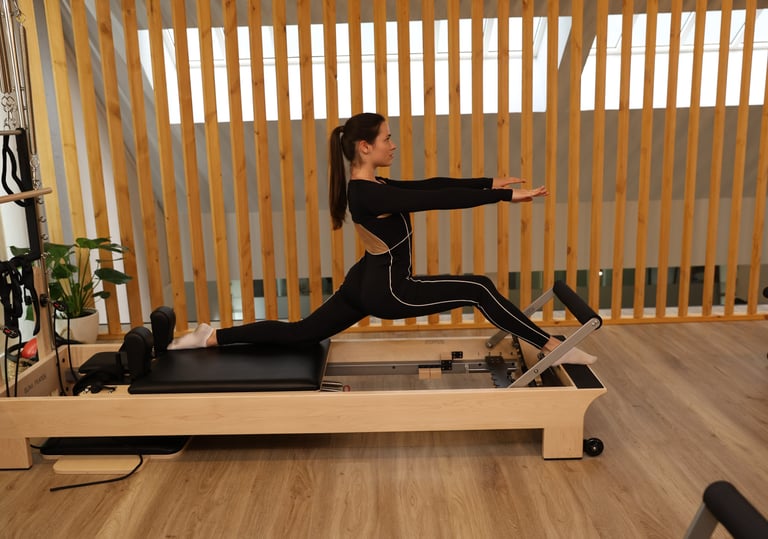 Uma mulher a realizar um alongamento em abertura no reformer num estúdio moderno 