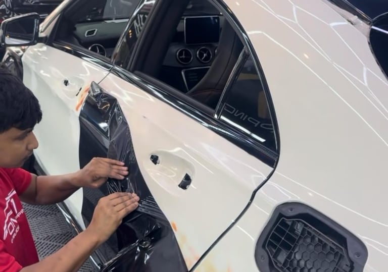 Technician removing old vinyl wrap film from car door panel