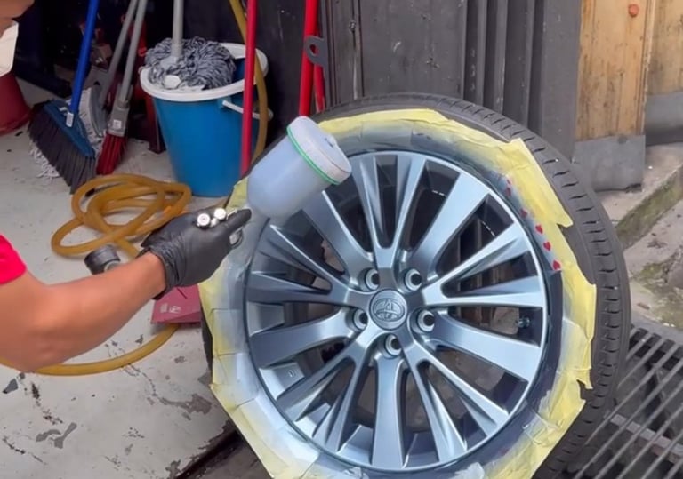 Technician spray wrapping car wheel rim in matte silver finish