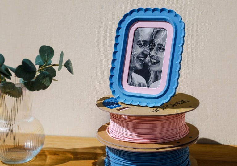 3D printable photo frame on desk with stand and matching colored filament spools