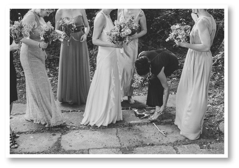 Bridesmaids standing together while one is fixing her shoe strap.
