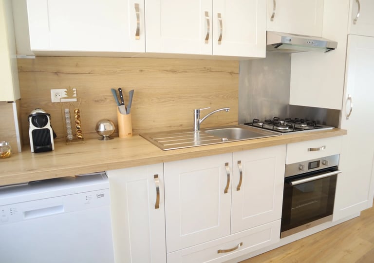 Cuisine équipée moderne avec four, plaques, lave-vaisselle et plan de travail en bois