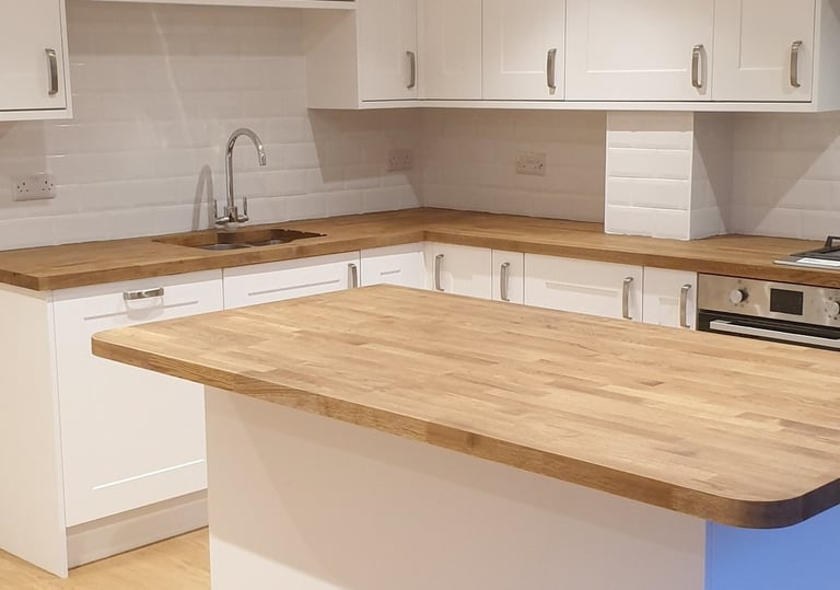 Modern white kitchen featuring a solid oak wood island countertop and matching hardwood flooring.