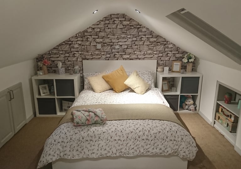 Cozy attic bedroom with a stone feature wall, sloped ceilings, and a white bed with yellow pillows.