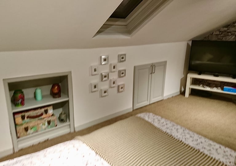 Cozy attic bedroom with sloped ceilings, built-in shelving, wall art, and a flat-screen TV.