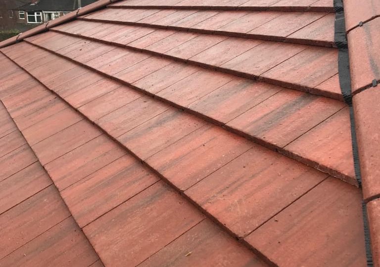 Red interlocking clay roof tiles installed on a residential house hip roof with ridge details.