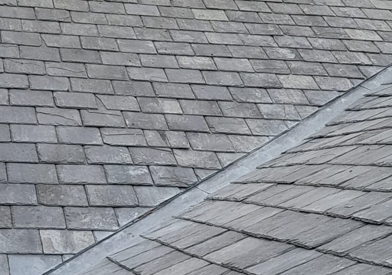 A weathered grey slate roof featuring a lead valley gutter and decorative ridge tiles.