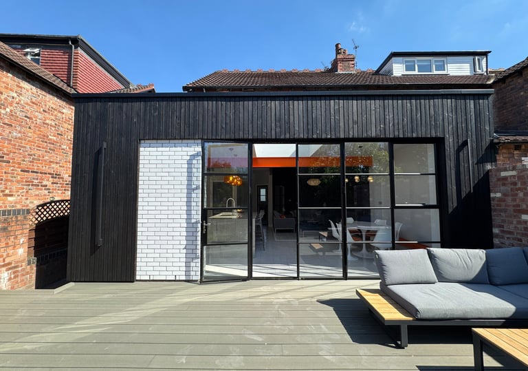 Modern home extension featuring black timber cladding and large glass Crittall doors opening onto a wooden deck.