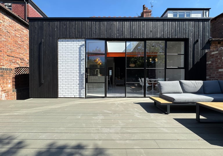 Modern home extension with black timber cladding, sliding glass doors, and a spacious outdoor composite deck.