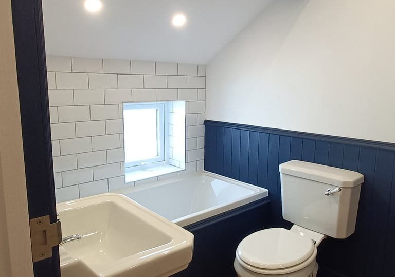 Modern attic bathroom with white bathtub, pedestal sink, and blue wood paneling.