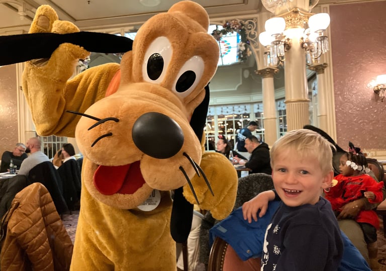 Pluto posing for a photo with a delighted little boy at Disneyland Paris Character Dinner