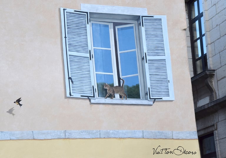 Fenêtre en trompe-l'oeil à Moirans-en-Montagne: un chat au bord d'une fenêtre regarde un oiseau.