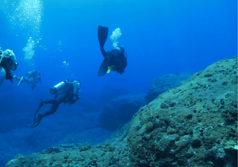 Scuba divers exploring a deep blue ocean reef with oxygen tanks and diving gear.
