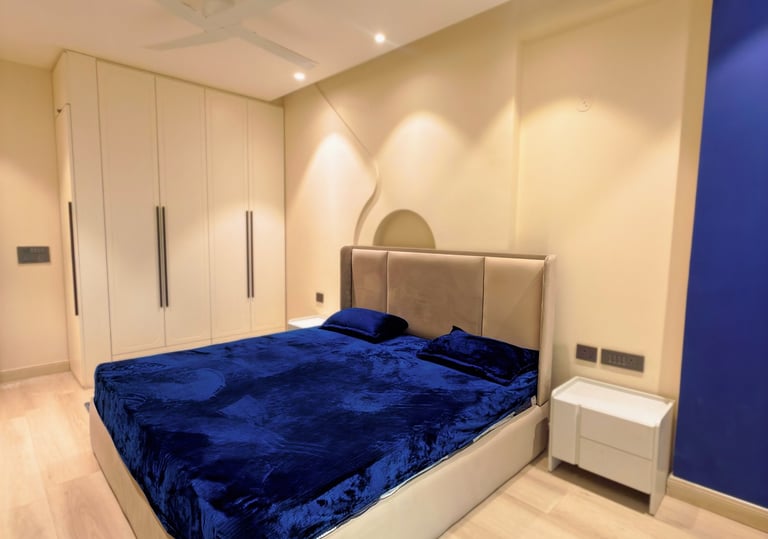 Modern bedroom with a cobalt blue velvet bedspread, beige upholstered headboard, and minimalist white wardrobe.