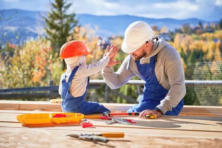 un père et son fils en tenue de travail s'amusant à construire une terrasse en bois