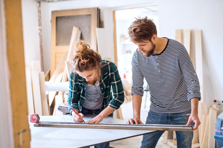 Une femme et un homme en train de mesurer une planche de bois