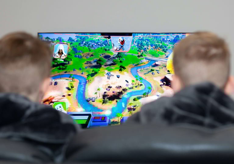 Two people playing the Fortnite video game on a large TV screen featuring a map with islands and rivers.