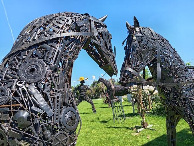Metal scrap art sculpture of two horse heads made from recycled tools and gears in a park.