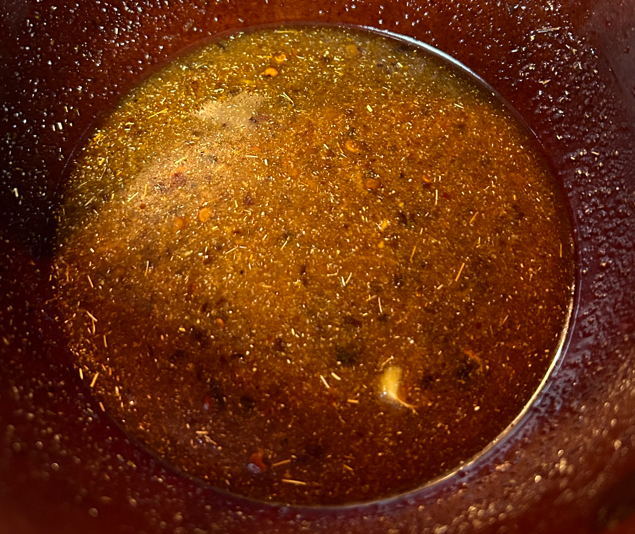 Brown sauce in a bowl full of spices and liquid.