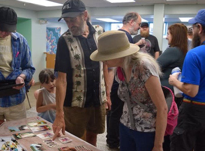 A group of people gathering around a table to look at a collection of small art cards at a community event.
