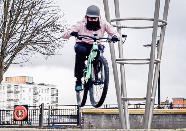 A bearded man in a helmet in mid-air during bike jump.