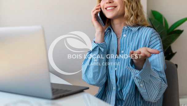 une dame avec une chemise bleu rayé et blanche appel le service SAV de bois local Grand Est