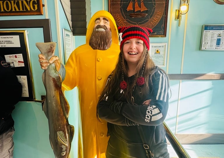 girl standing next to a fisherman statue in a yellow raincoat holding a fish 