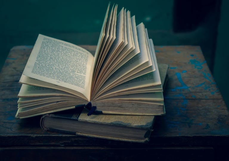 An open vintage hardcover book with fanned pages resting on an antique wooden table.